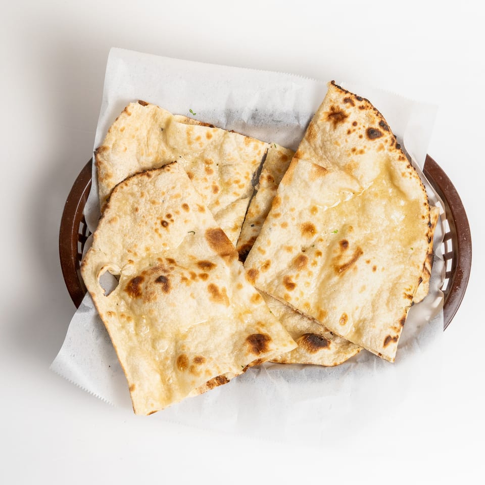 Golden-brown naan bread pieces, lightly brushed with butter, served in a brown basket with white parchment paper.