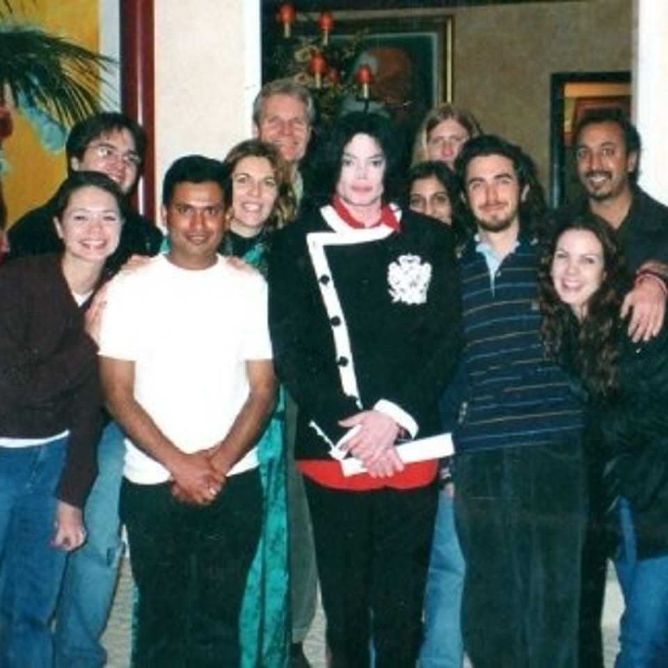 Group of diverse adults posing indoors near a palm plant and festive decorations.