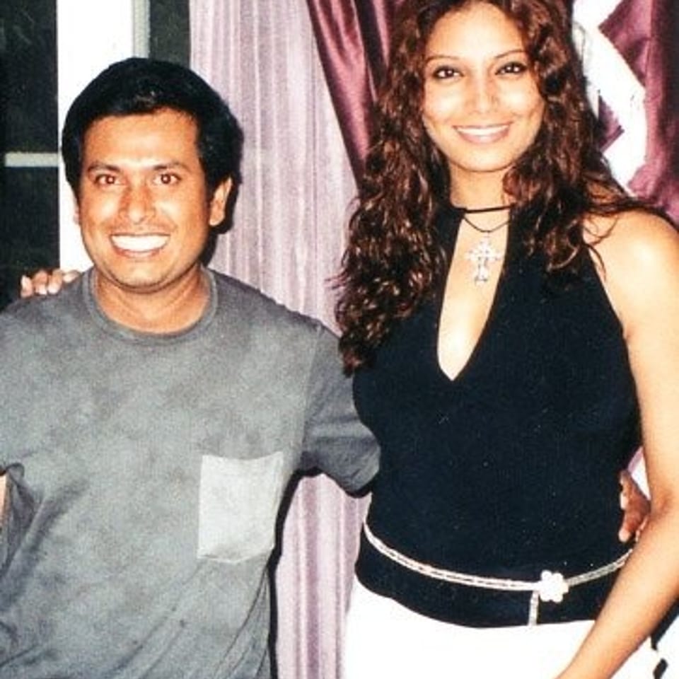 Smiling man and woman pose together in front of burgundy and white curtains at a restaurant event.