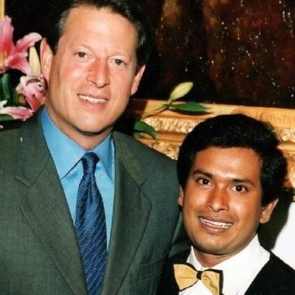 Two formally dressed men pose together, one wearing a green suit and the other a black tuxedo with a bow tie.