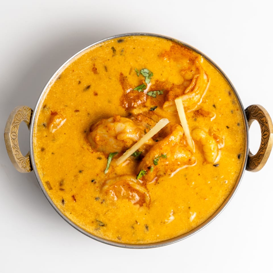 Creamy orange curry with shrimp and ginger slices in a metal bowl with ornate handles.