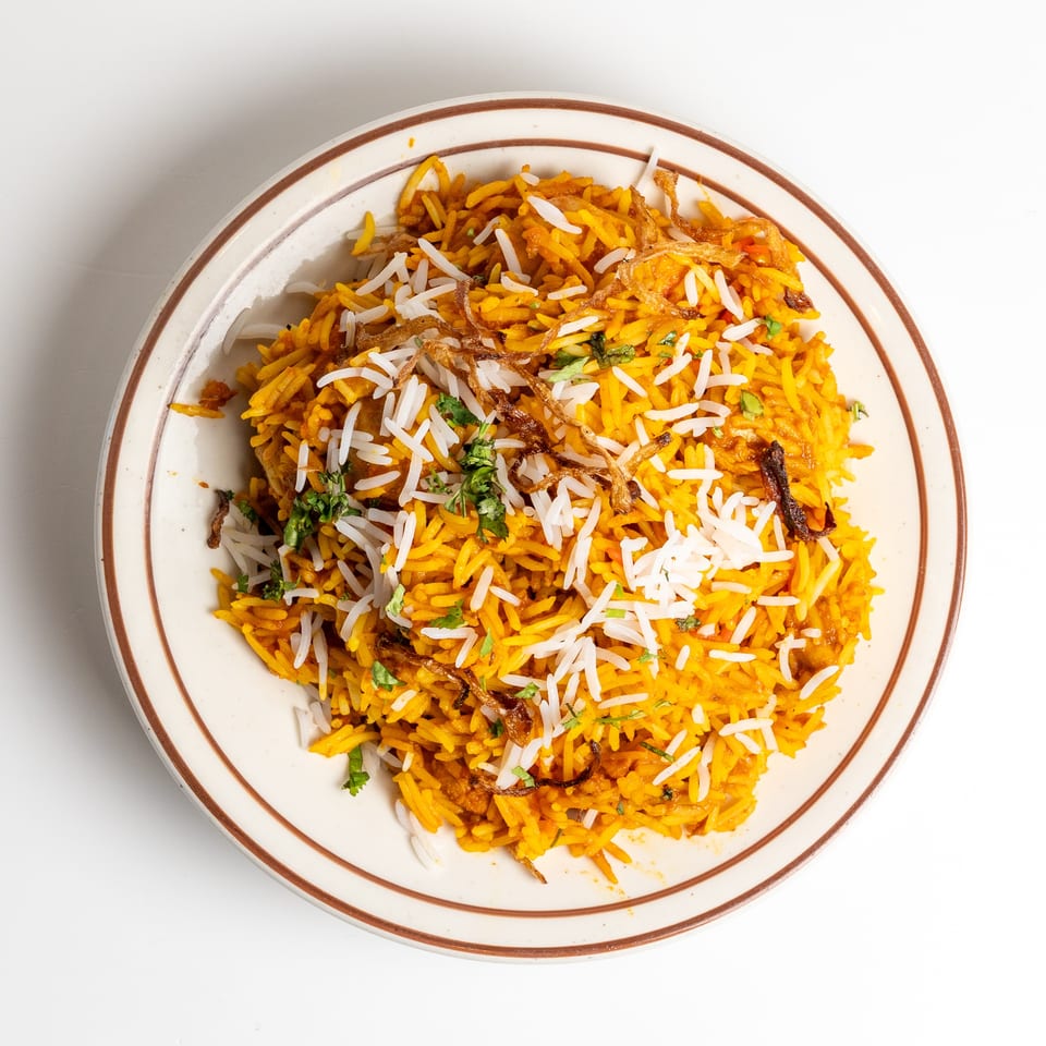 Overhead view of a plate of vibrant orange biryani rice, garnished with white rice, fried onions, and cilantro.