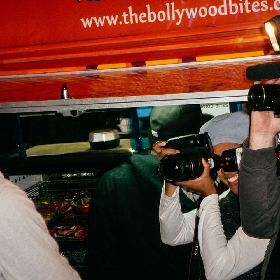 Two videographers film a man in front of The Bollywood Bites food truck.