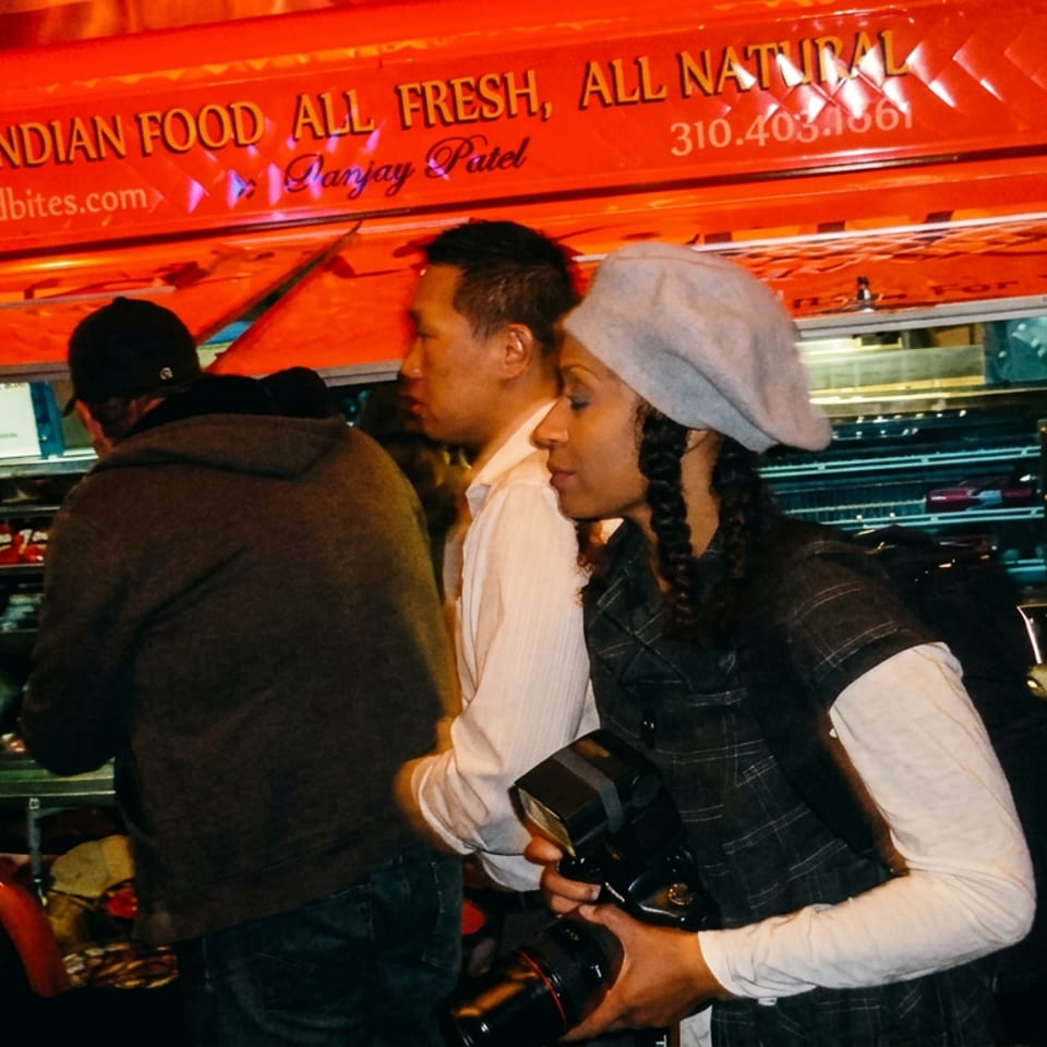 People gather around a red food truck with "Authentic Indian Food" written on its side at night.