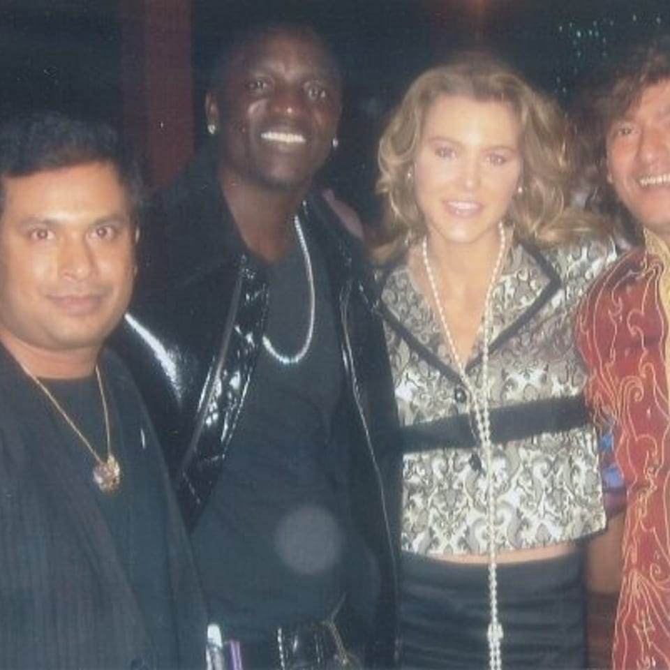 Four people, including a smiling woman and man in colorful clothing, pose together in a dimly lit indoor venue.